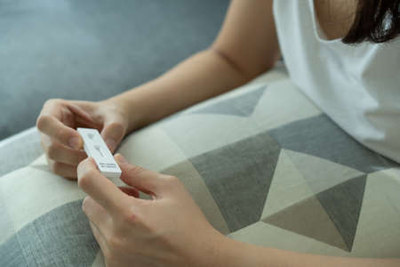 Asian young woman with hygiene protective face mask using  antigen rapid test kit - ag test kit at home.  antigen rapid test.の写真素材