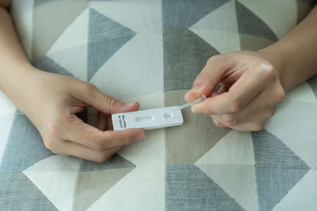 Asian young woman with hygiene protective face mask using  antigen rapid test kit - ag test kit at home.  antigen rapid test.の写真素材