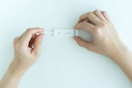 Asian young woman with hygiene protective face mask using SARS 2019-nCoV COVID-19 coronavirus antigen rapid test kit - ag test kit at home. COVID-19 antigen rapid test.の写真素材