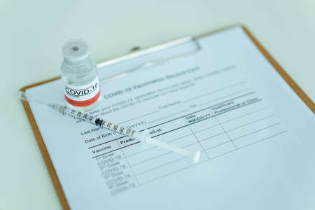 COVID-19 or coronavirus vaccine in a bottle and needle with the COVID-19 vaccination record document close up with copyspace.の写真素材