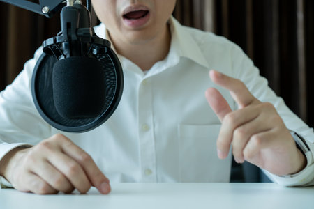 Unrecognizable Asian businessman making his online podcast from home, a businessman talking on the online radio station and using professional condenser microphone. Audio live streaming concept.の写真素材