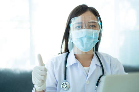 Beautiful Asian doctor wear a protective face shield and face mask while working in the hospital portrait. Young Asian doctor in hospital looking at camera. Health care working portrait.の写真素材