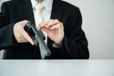 Unrecognizable Asian businessman draw the gun from gun holder inside his suit close up. Businessman or agent in black suit showing the revolver handgun on the table.の写真素材