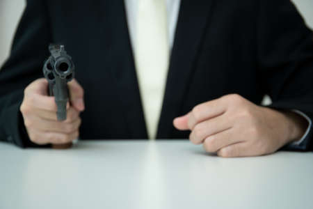 Unrecognizable Asian businessman draw the gun from gun holder inside his suit close up. Businessman or agent in black suit showing the revolver handgun on the table.の写真素材
