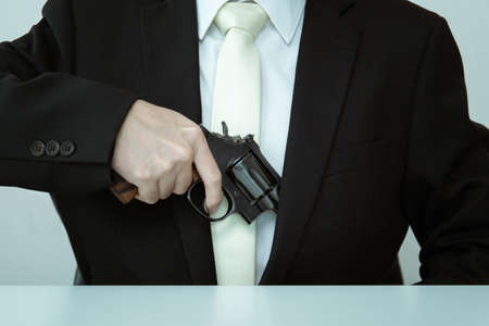 Unrecognizable Asian businessman draw the gun from gun holder inside his suit close up. Businessman...