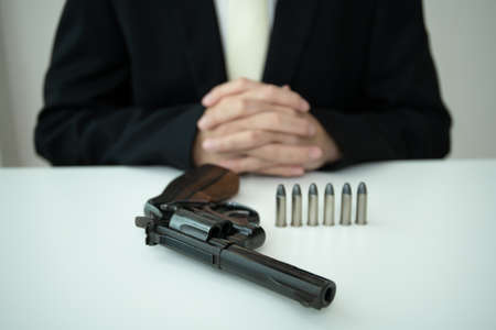 Unrecognizable Asian businessman draw the gun from gun holder inside his suit close up. Businessman or agent in black suit showing the revolver handgun on the table.の写真素材