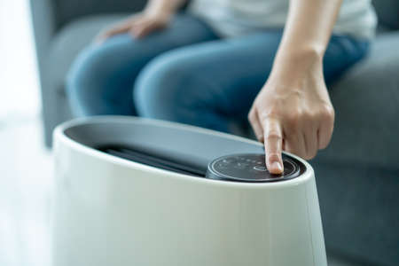 Asian woman turning on and using the modern air purifier while staying in the living room, air...