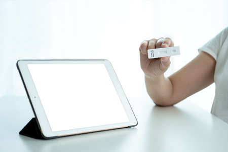 Mockup modern tablet with empty screen isolated with clipping path. Asian young woman using tablet for online video call with a doctor after her COVID-19 antigen testing result was positive.の写真素材