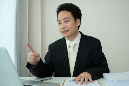 Asian young businessman making an online video conference while working at home due to coronavirus or COVID-19 pandemic. Asian businessman using laptop for online meeting.の写真素材