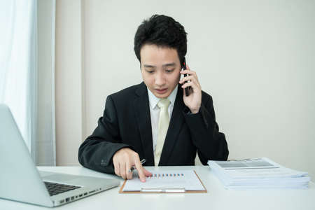 Asian young businessman making an online video conference while working at home due to coronavirus or COVID-19 pandemic. Asian businessman using laptop for online meeting.の写真素材