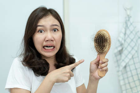 Asian young woman worried about hair fall problem, serious Asian beautiful girl showing a falling hair on a comb brush close up with copy space. Young woman worried about hair fall problem.の写真素材
