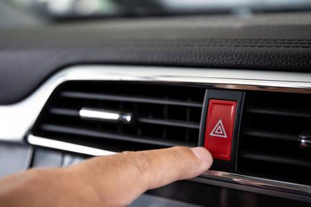 Driver pressing on hazard button on a car dashboard close up with audio and entertainment control...
