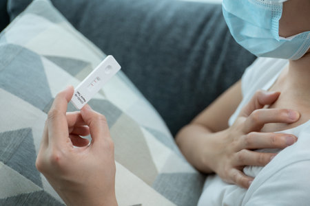 Asian young woman with hygiene protective face mask using SARS 2019-nCoV COVID-19 coronavirus antigen rapid test kit - ag test kit at home. COVID-19 antigen rapid test.の写真素材