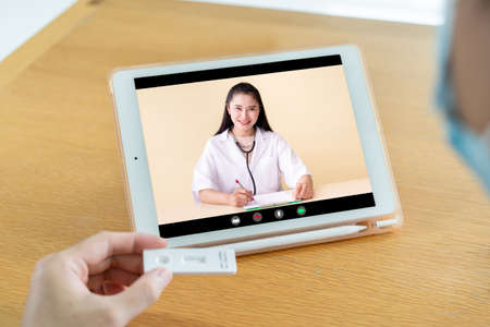 Asian young man showing the COVID-19 or Coronavirus antigen - ag testing result to a doctor in the online video call, tele - online medication service.の写真素材