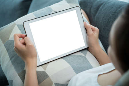 Isolated with clipping path on mockup tablet screen, woman using a tablet while relaxing or sitting on sofa in living room and browsing the internet - social media. Woman  surfing the social network.の写真素材