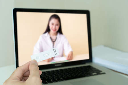 Unrecognizable Asian young man having a health problem and consulting with doctor via online medication service. Man got a COVID-19 disease and chat to doctor on a video call on laptop.の写真素材