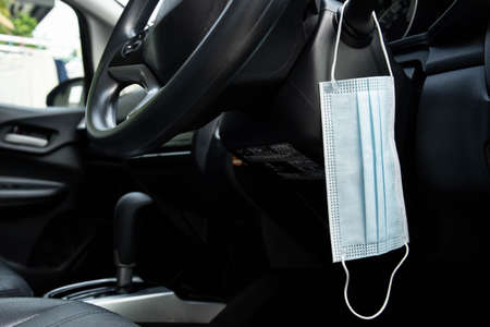 Medical face mask hanging on the headlight controller stick in a modern vehicle close up. Health...