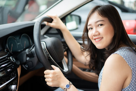 Happy Asian young woman driver sitting on the driver seat in the luxury modern car close up with copyspace. Asian girl sitting in the car cockpit and smiling to camera. Joyful woman driving a car.の写真素材