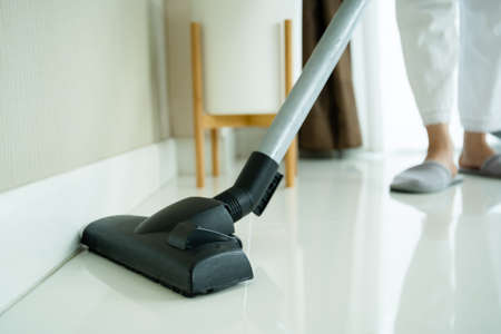 Asian young housekeeper using vacuum machine to clean a dirty floor in the living room close up with copyspace. Housewife vacuuming a floor and sofa in living room.の写真素材