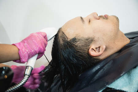 Asian young man having a hair care treatment and hair washing service at hair salon.の写真素材