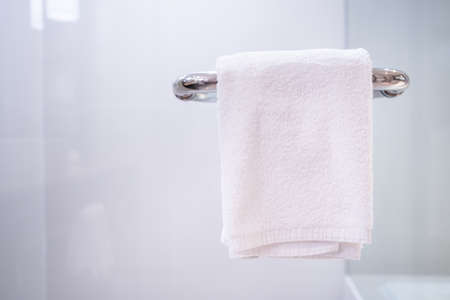 Sanitized white towel hanging on the shower room hand rail close up with copyspace, bath in background. Luxurious bath and shower room in hotel. Healthcare - wellness concept.の写真素材