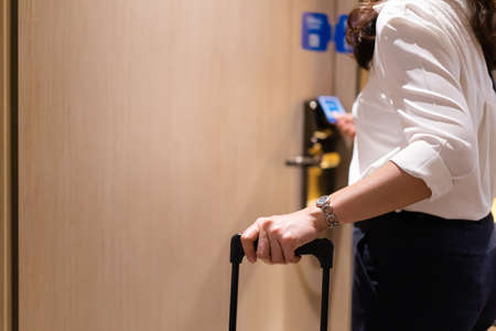 Unrecognizable businesswoman in smart casual carrying a hard suitcase to the room in hotel and using room keycard to unlock the door.の写真素材