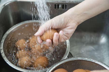 Unrecognizable Asian housewife washing a raw eggs in the sink close up, woman sanitizing and preparing a dirty eggshell before cooking in kitchen.の写真素材