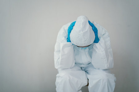 Stressful - worried Asian medication staff sitting on a chair against the wall, healthcare worker hard working in hospital. Overworked health care worker - nurse feels tired.の写真素材
