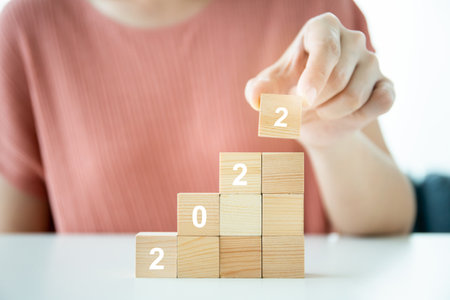 Step up on wood blocks ladder placed the word 2022 for 2022 new year celebration, unrecognizable young woman placing a wood block showing the year 2022.の写真素材
