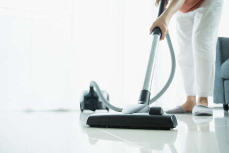 Asian young housekeeper using vacuum machine to clean a dirty floor in the living room close up with copyspace. Housewife vacuuming a floor and sofa in living room.の写真素材