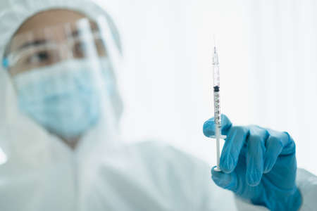 Unrecognizable specialist doctor in a medical PPE suit showing and looking at an injection needleの写真素材