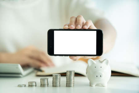 blank screen smartphone. Money saving and investment concept. Young woman showing a mockup empty blank screen of smartphone with her money saving.の写真素材