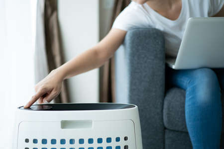 Asian young woman working in home office and using an air purifier, a girl sitting on sofa and using laptop.の写真素材