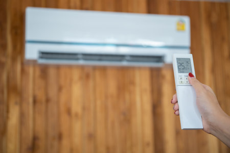 Modern air conditioner hanging on the vintage wooden wall with copyspace. Unrecognizable woman turning on an air conditioner by using remote control.の写真素材