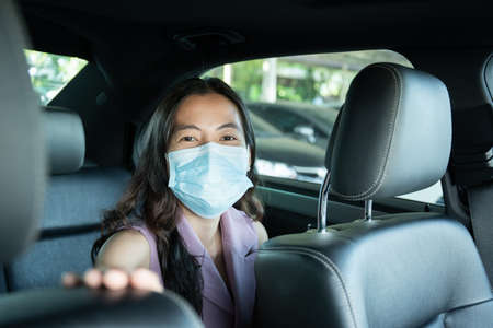 Beautiful Asian businesswoman wear a hygiene protective face mask taking a back seat in taxi portrait, happy Asian woman passenger with face mask traveling by using taxiの写真素材