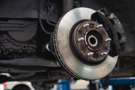 Old caliper break and disc break in a vehicle, an old car lifted up on the hydraulic ramp for inspection and maintenance in garage.の写真素材