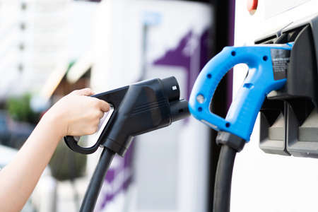 Unrecognizable Asian woman holding aa DC - CCS type 2 EV charging connector at EV charging station, woman preparing an EV - electric vehicle charging connector for recharge a vehicle.の写真素材