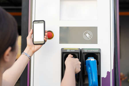 Asian woman preparing her electric vehicle - EV for changing at the EV charging station, woman using application on a smartphone to connect with EV charging station.の写真素材