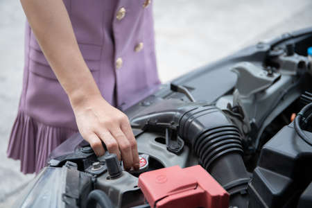 Unhappy beautiful Asian businesswoman standing in front of her broken vehicle beside the road, serious asian woman looking inside the broken car hood. Car accident and broken down.の写真素材