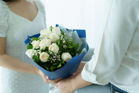 Happy Asian young couple in Valentine or anniversary stay together, man giving and surprise his wife a bouquet in their Valentine or Anniversary day. Husband and wife celebrating in Valentine day.の写真素材