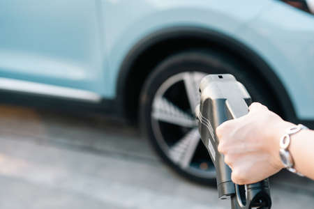 Unrecognizable Asian woman holding aa DC - CCS type 2 EV charging connector at EV charging station, woman preparing an EV - electric vehicle charging connector for recharge a vehicle.の写真素材
