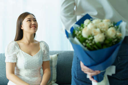 Happy Asian young couple in Valentine or anniversary stay together, man giving and surprise his wife a bouquet in their Valentine or Anniversary day. Husband and wife celebrating in Valentine day.の写真素材