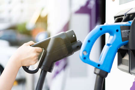 Unrecognizable Asian woman holding aa DC - CCS type 2 EV charging connector at EV charging station, woman preparing an EV - electric vehicle charging connector for recharge a vehicle.の写真素材