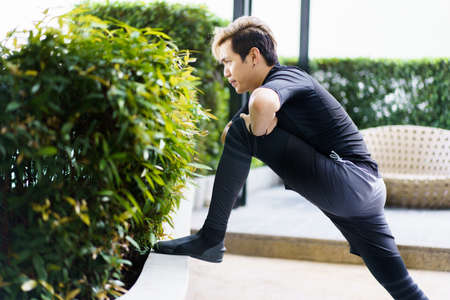 Happy Asian young sportsman doing a lower and upper body stretching before making an exercise in a park, stretching and workout concept. Sport man making a cardio and weight training workout.の写真素材