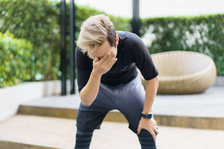 Tired Asian young sportsman resting after made a cardio and weight exercise, Asian young man in sport clothes resting after jogging outdoor close up.の写真素材