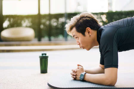 Active Asian young man making an outdoor body weight exercise close up, sportsman doing body weight workout by pushup and plank. Asian sportsman exercising for muscle and body building.の写真素材