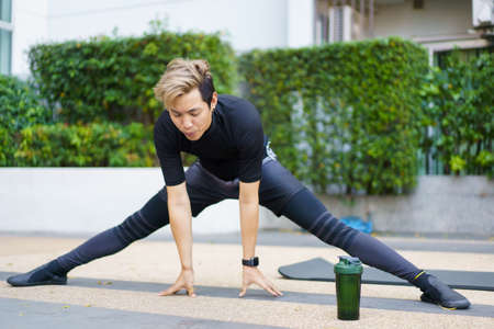 Happy Asian young sportsman doing a lower and upper body stretching before making an exercise in a park, stretching and workout concept. Sport man making a cardio and weight training workout.の写真素材