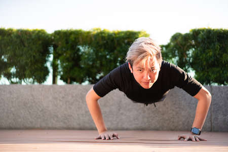 Active Asian young man making an outdoor body weight exercise close up, sportsman doing body weight workout by pushup and plank. Asian sportsman exercising for muscle and body building.の写真素材
