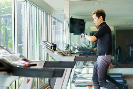 Active Asian sportsman making a cardio exercise by running on the treadmill machine in a fitness or gym, healthy sport man doing a cardio workout.の写真素材
