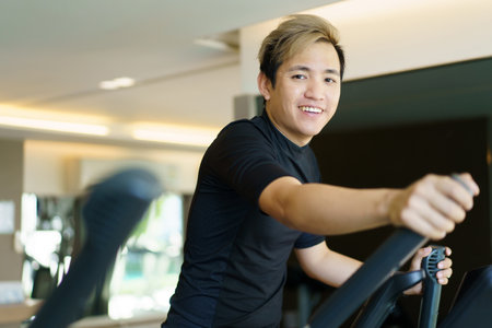 Active Asian young man making a cardio exercise on the elliptical exercise machine in the gym. Fat burn and body muscle building. bodybuilding workout concept.の写真素材